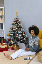 Lächelnde Frau mit Laptop unter dem Weihnachtsbaum zu Hause - GIOF15307