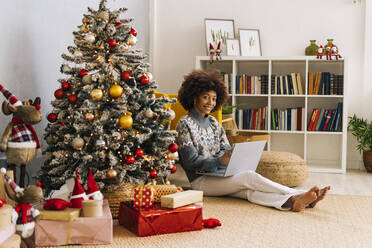 Glückliche junge Frau mit Laptop unter dem Weihnachtsbaum zu Hause - GIOF15309