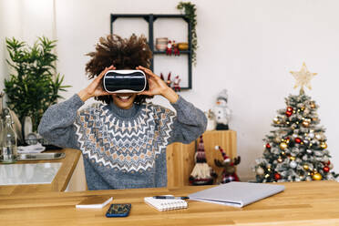 Smiling woman wearing virtual reality simulator sitting at home - GIOF15326