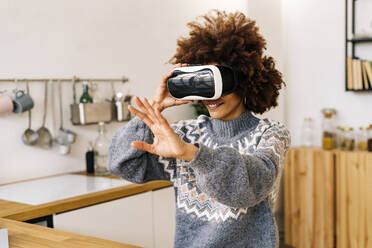 Smiling young woman wearing virtual reality simulator gesturing at home - GIOF15328