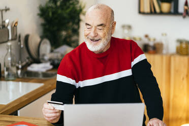 Lächelnder älterer Mann mit Kreditkarte beim Online-Shopping mit dem Laptop zu Hause - GIOF15360