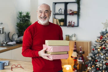 Glücklicher älterer Mann mit Geschenkboxen am Tisch zu Hause - GIOF15369