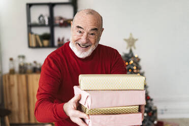 Smiling senior man giving gift boxes at home - GIOF15371