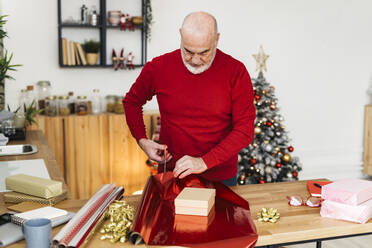 Älterer Mann packt Weihnachtsgeschenke auf dem Tisch zu Hause ein - GIOF15377