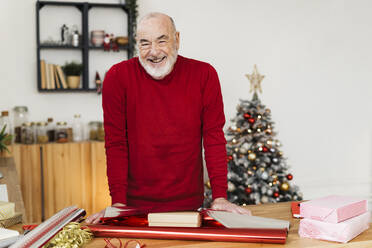 Glücklicher älterer Mann mit Geschenkpapier und Schachteln auf dem Tisch zu Hause - GIOF15381