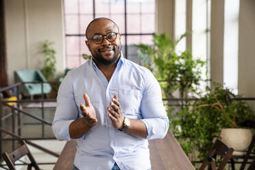 Smiling businessman wearing eyeglasses gesturing at office - VPIF05621