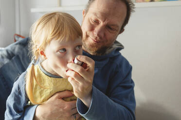 Father helping daughter using asthma inhaler at home - IHF00771