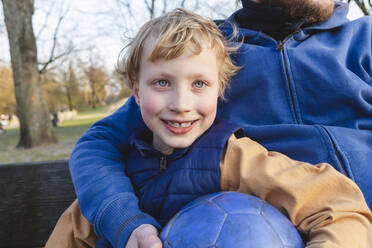 Smiling son with father sitting on bench at park - IHF00772