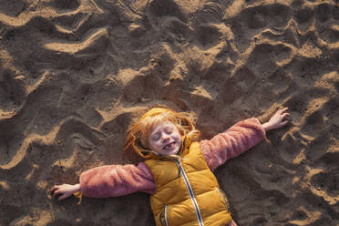 Playful girl with blond hair lying on sand - IHF00774