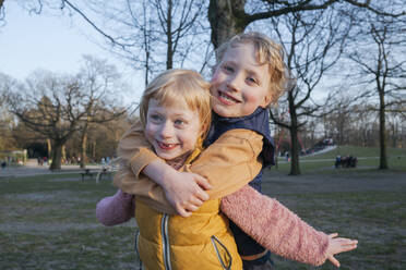Verspielter Junge umarmt Schwester von hinten im Park - IHF00775