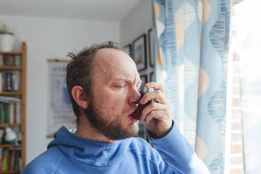 Man with eyes closed using asthma inhaler at home - IHF00777