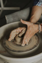 Hands of young man molding clay on potter's wheel in workshop - SSGF00624