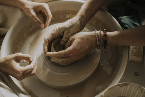 Hände eines Ausbilders, der einem jungen Mann das Formen einer Schale auf der Töpferscheibe in einer Werkstatt beibringt - SSGF00628