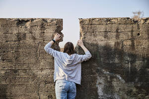Young woman looking through gap in concrete wall - MMIF00278