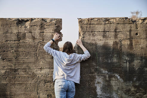 Young woman looking through gap in concrete wall - MMIF00278