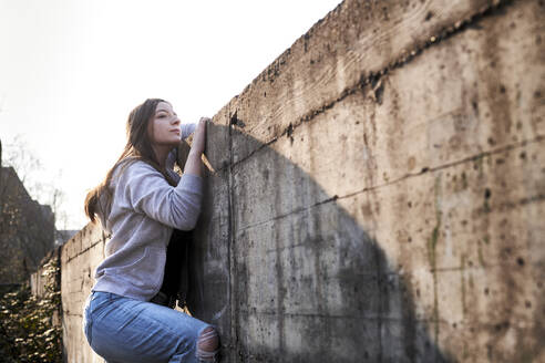 Neugierige junge Frau schaut über eine Betonmauer - MMIF00280