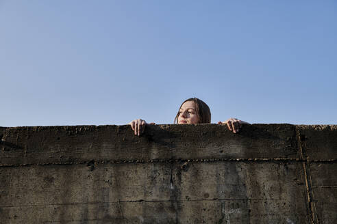 Young woman looking over concrete wall - MMIF00283