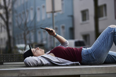 Young woman lying on table tennis table reading text messages - MMIF00288