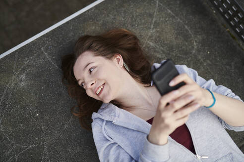 Young woman lying on table tennis table holding smartphone - MMIF00291