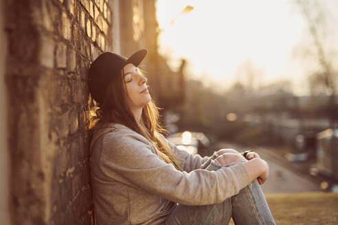 Young woman leaning on brick wall with eyes closed - MMIF00299