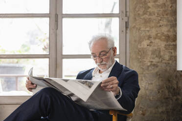 Älterer Mann liest zu Hause vor dem Fenster sitzend Zeitung - EIF03668