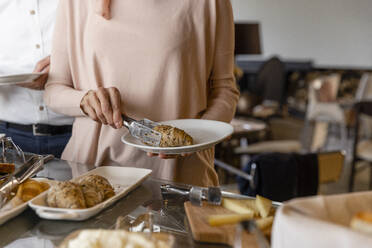 Ältere Frau nimmt Croissant vom Frühstücksbuffet von einem Mann in einem Boutique-Hotel - EIF03704
