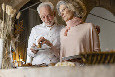 Lächelnde ältere Frau gibt einem Mann, der am Frühstücksbuffet in einem Boutique-Hotel steht, ein Croissant - EIF03705