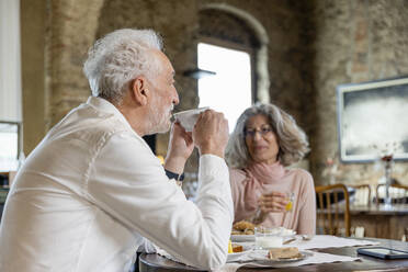 Lächelndes älteres Paar trinkt Kaffee und sitzt mit einer Frau am Tisch in einem Boutique-Hotel - EIF03708