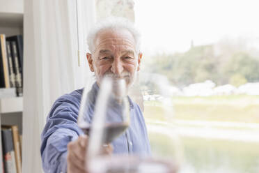 Älterer Mann stößt zu Hause am Fenster mit einem Weinglas an - EIF03742