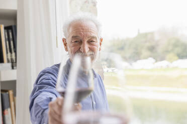 Senior man toasting wineglass by window at home - EIF03742