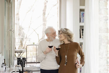 Happy senior couple with wineglasses standing in hotel apartment - EIF03752