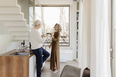 Senior couple toasting wineglasses in kitchen at hotel apartment - EIF03756