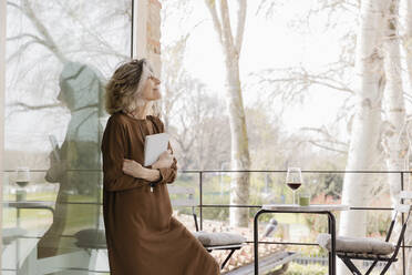 Ältere Frau mit Buch auf dem Balkon eines Hotelappartements - EIF03761