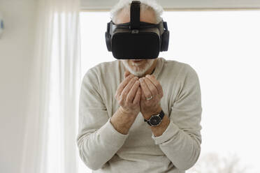 Ein älterer Mann in einem Virtual-Reality-Simulator steht mit gefalteten Händen in einem Boutique-Hotel - EIF03763