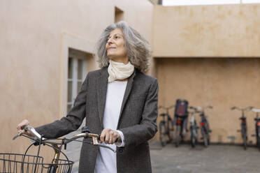 Senior woman standing with bicycle in front of building - EIF03779