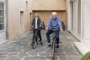 Smiling senior couple riding bicycles on footpath - EIF03782