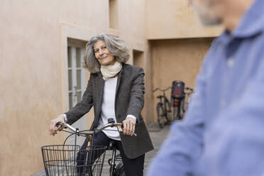 Lächelnde ältere Frau mit Fahrrad, die einen Mann vor einem Gebäude ansieht - EIF03784