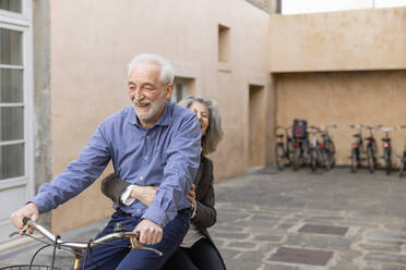 Ältere Frau sitzt mit einem Mann auf dem Fahrrad vor einem Gebäude - EIF03787