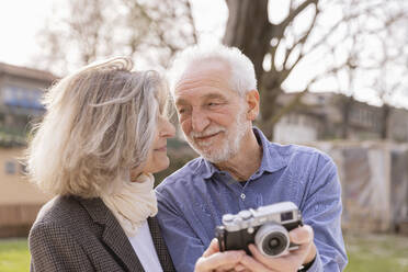 Glückliches älteres Paar mit Kamera, das sich an einem sonnigen Tag ansieht - EIF03793