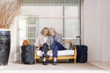 Fröhliches älteres Ehepaar auf Bank sitzend, Gepäck vor einem Glas - EIF03804