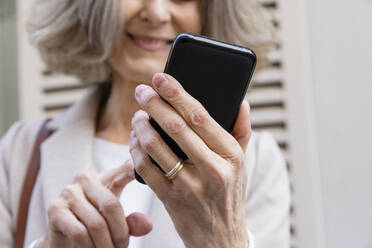 Lächelnde ältere Frau, die mit ihrem Mobiltelefon im Internet surft - EIF03808