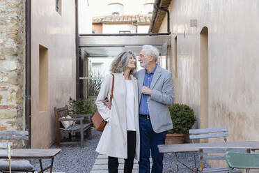 Happy senior couple looking at each other standing at hotel courtyard - EIF03811