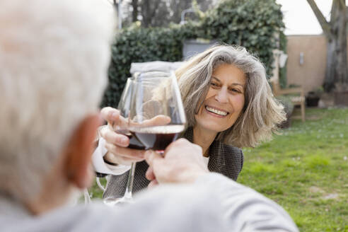 Glückliches älteres Paar stößt im Garten sitzend mit Weingläsern an - EIF03815
