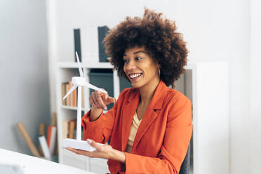 Lächelnde Geschäftsfrau mit Windmühlenmodell im Büro sitzend - GIOF15433