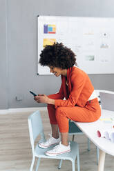 Smiling businesswoman text messaging through mobile phone sitting on desk in office - GIOF15438