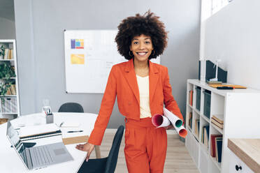 Lächelnde Geschäftsfrau mit Afrofrisur, die einen Bauplan im Büro hält - GIOF15443