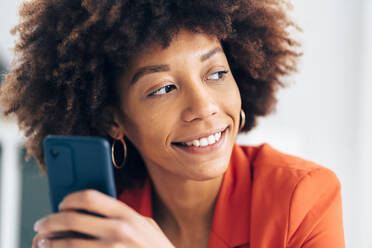 Lächelnde Geschäftsfrau mit Afrofrisur, die ein Mobiltelefon hält - GIOF15455