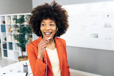 Happy businesswoman talking through in-ear headphones at office - GIOF15471