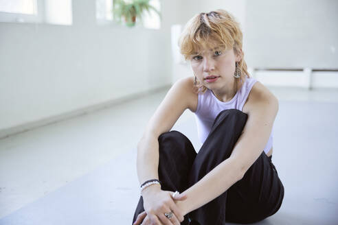 Young blond woman sitting with hands clasped on floor - SUF00671