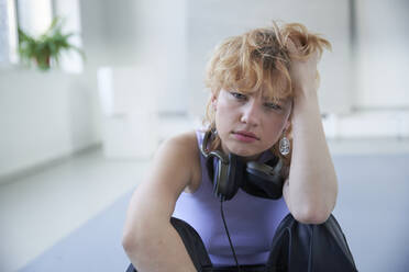 Junge Frau mit Kopfhörern, sitzend mit der Hand im Haar - SUF00680